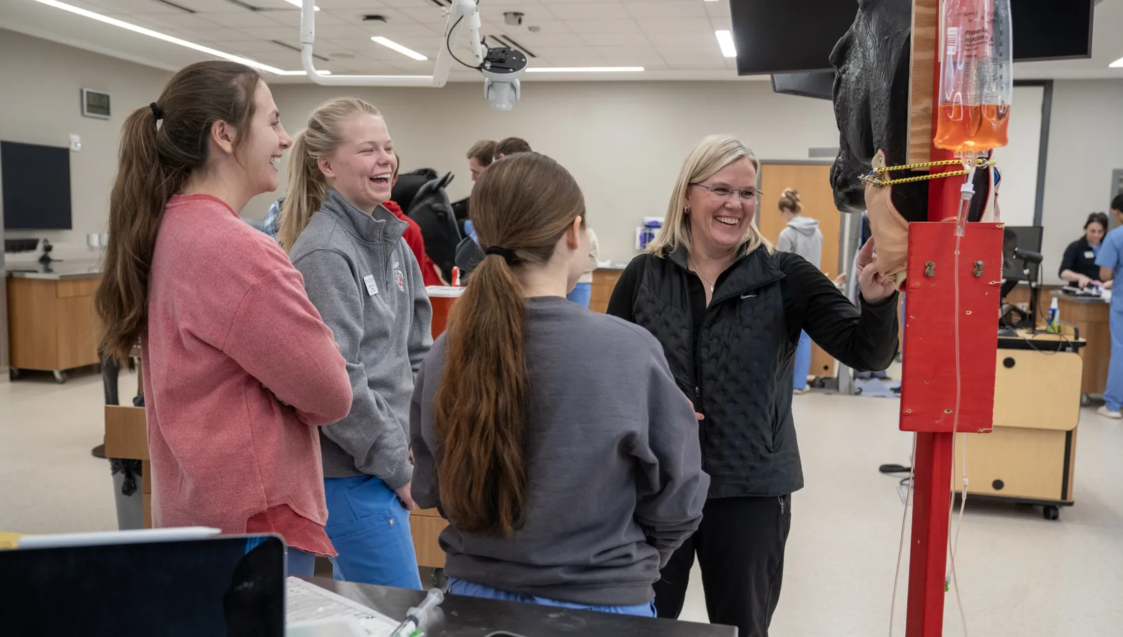 faculty member laughs with three female students while teaching in the clinical skills lab