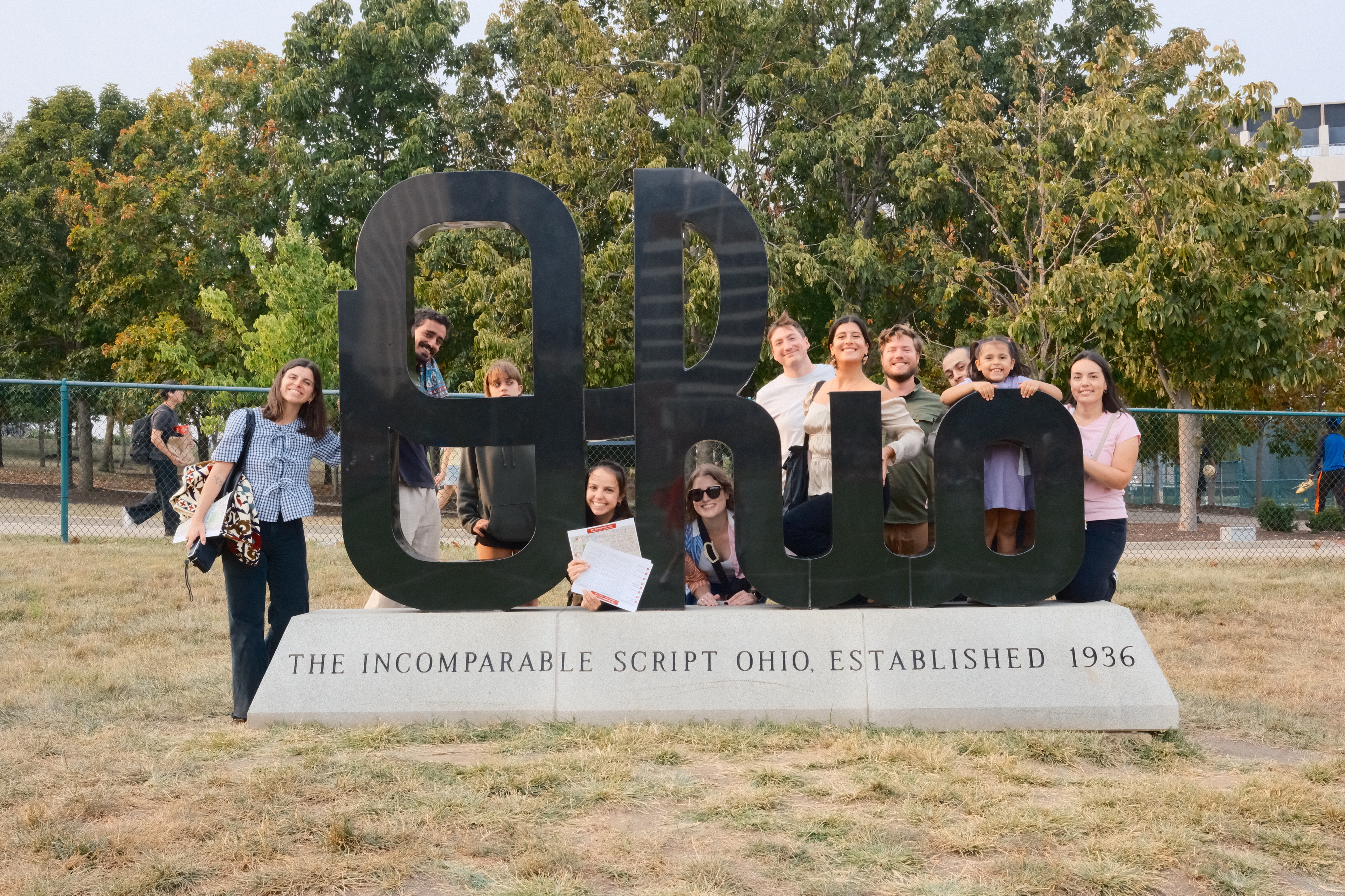 group of students posing with script OHIO sculpture on campus