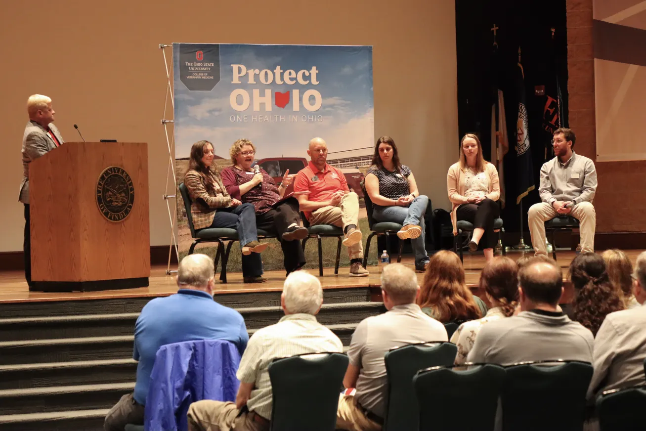Group of people on a stage talk into microphone to an audience