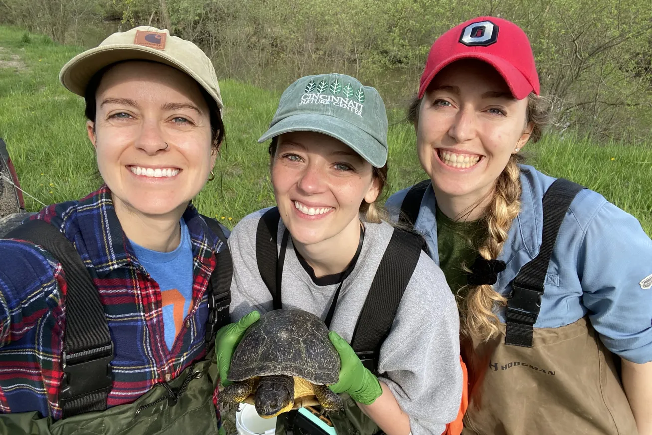 Three smiling students holding a less enthusiastic looking turtle. 
