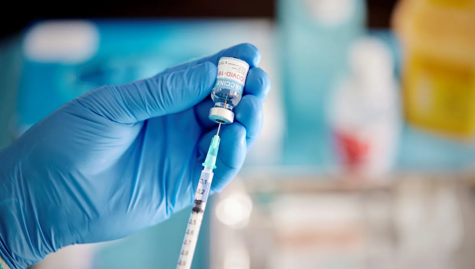 A healthcare Worker hands in surgical gloves pulling COVID-19 vaccine liquid from vial to vaccinate a patient