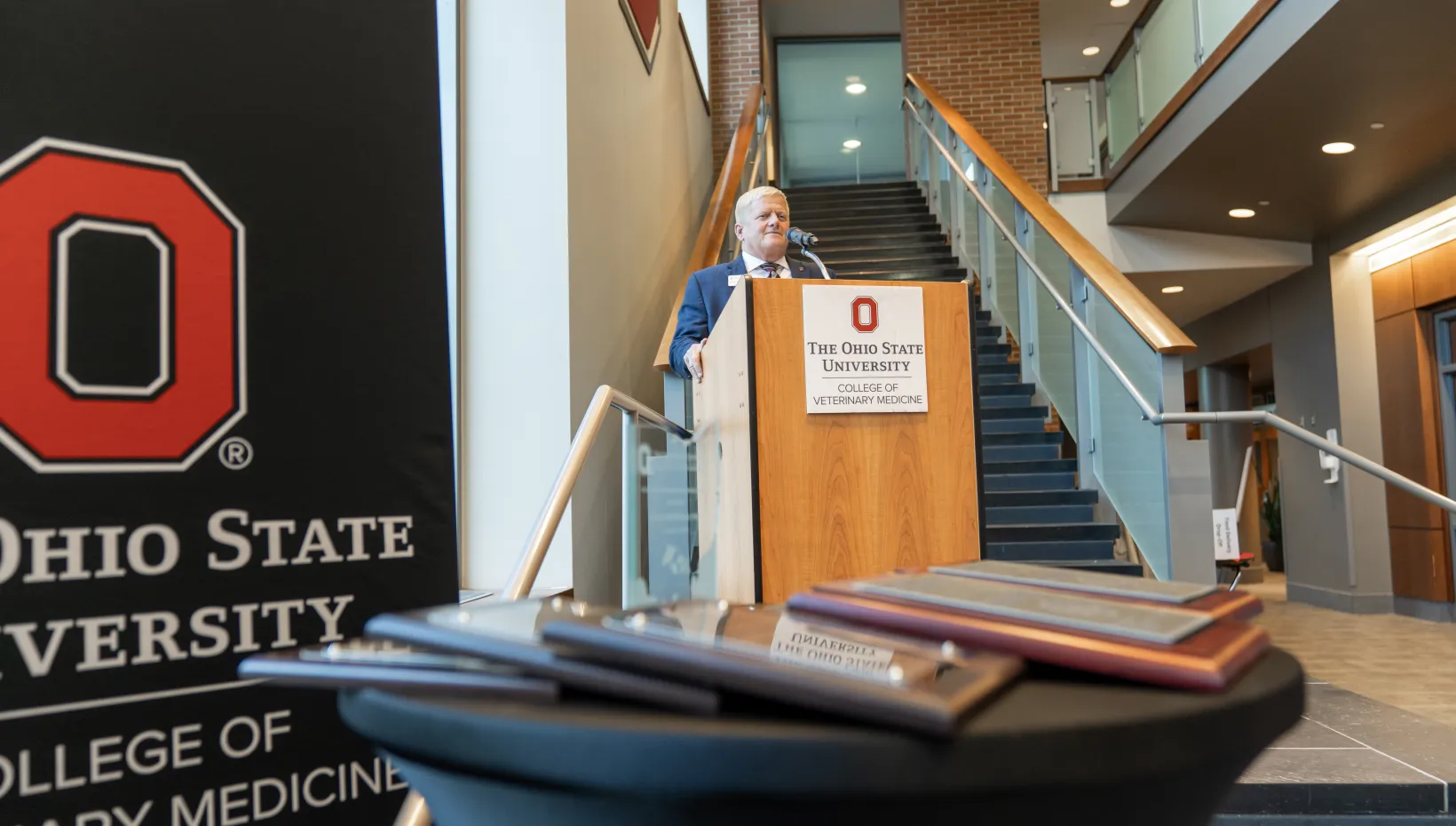 Dean Rustin Moore in background at podium, awards in foreground. 