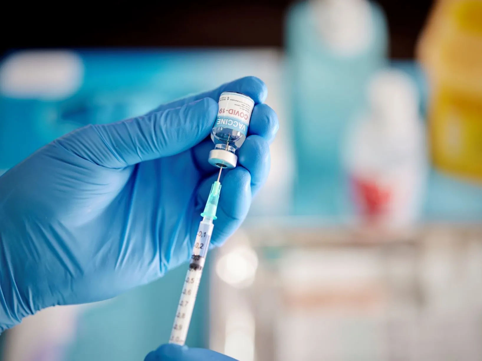 A healthcare Worker hands in surgical gloves pulling COVID-19 vaccine liquid from vial to vaccinate a patient