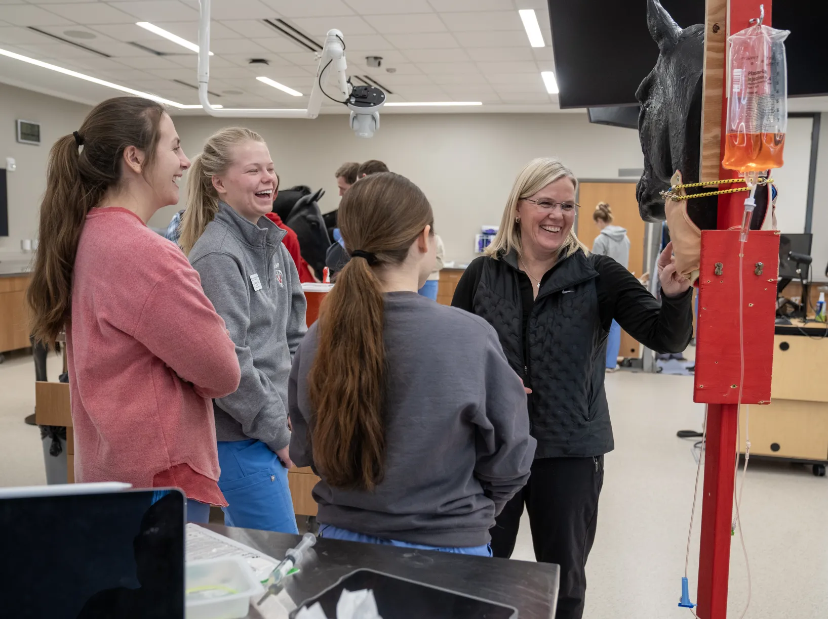 faculty member laughs with three female students while teaching in the clinical skills lab