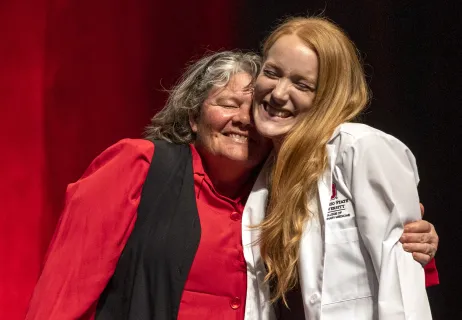 An older woman embracing a young woman who just received her white coat