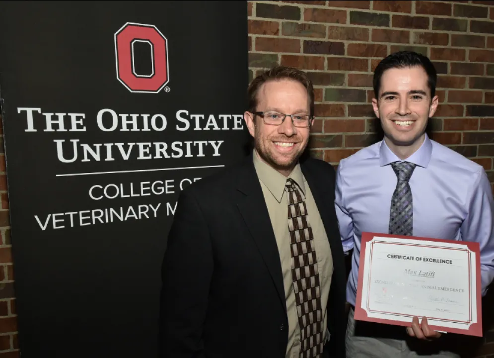 two smiling men, one holding an award