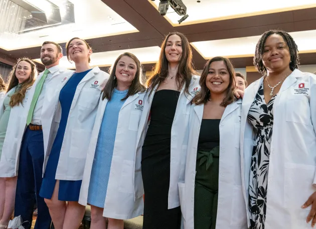 group of smiling students in white coats at ceremony